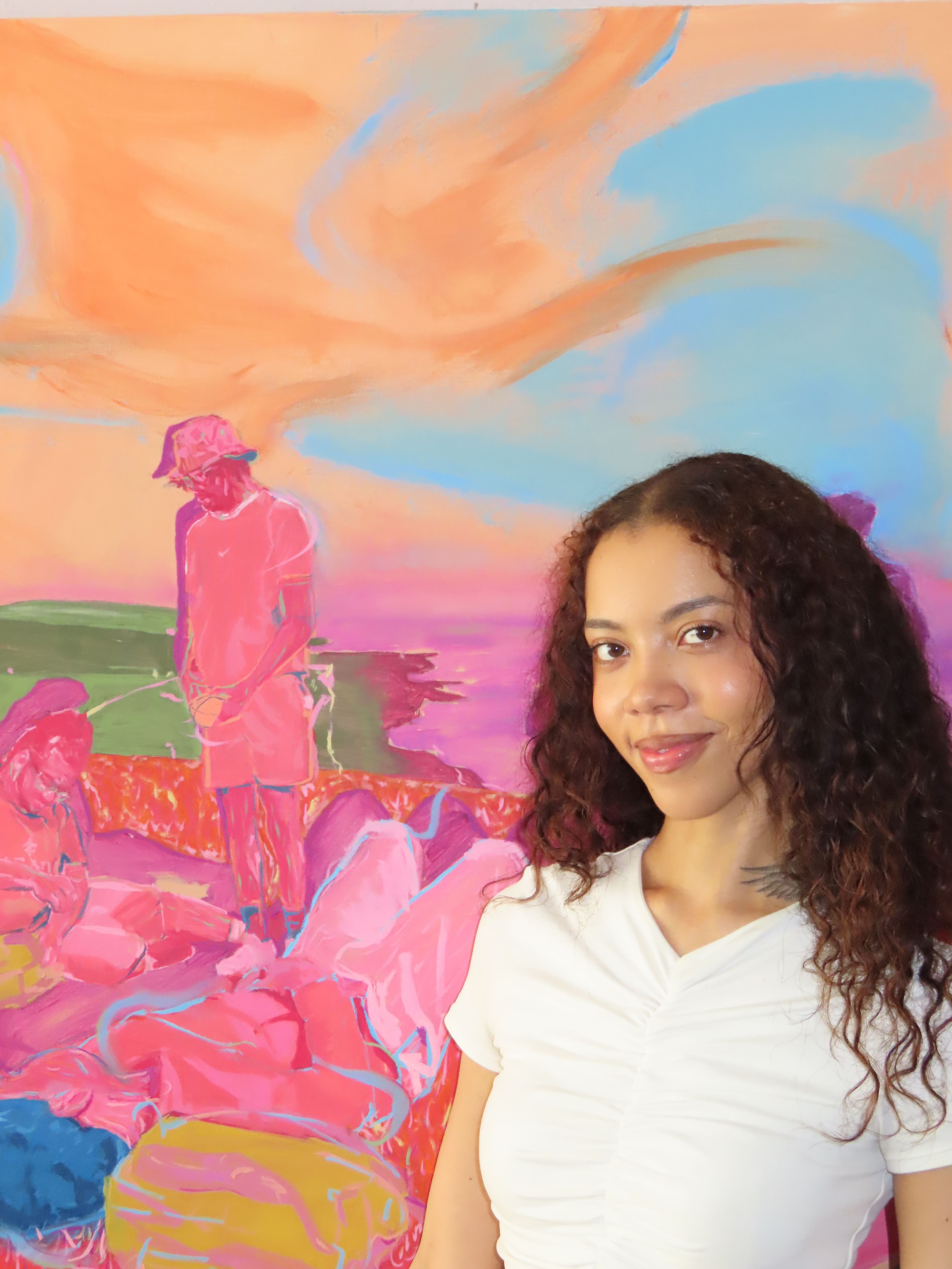 Loretta Yussuff in the studio in front of saturated colourful oil painting Wanderers, a figure holds a ball, two figures rest and a sweeping sky of blue and orange takes up most of the canvas